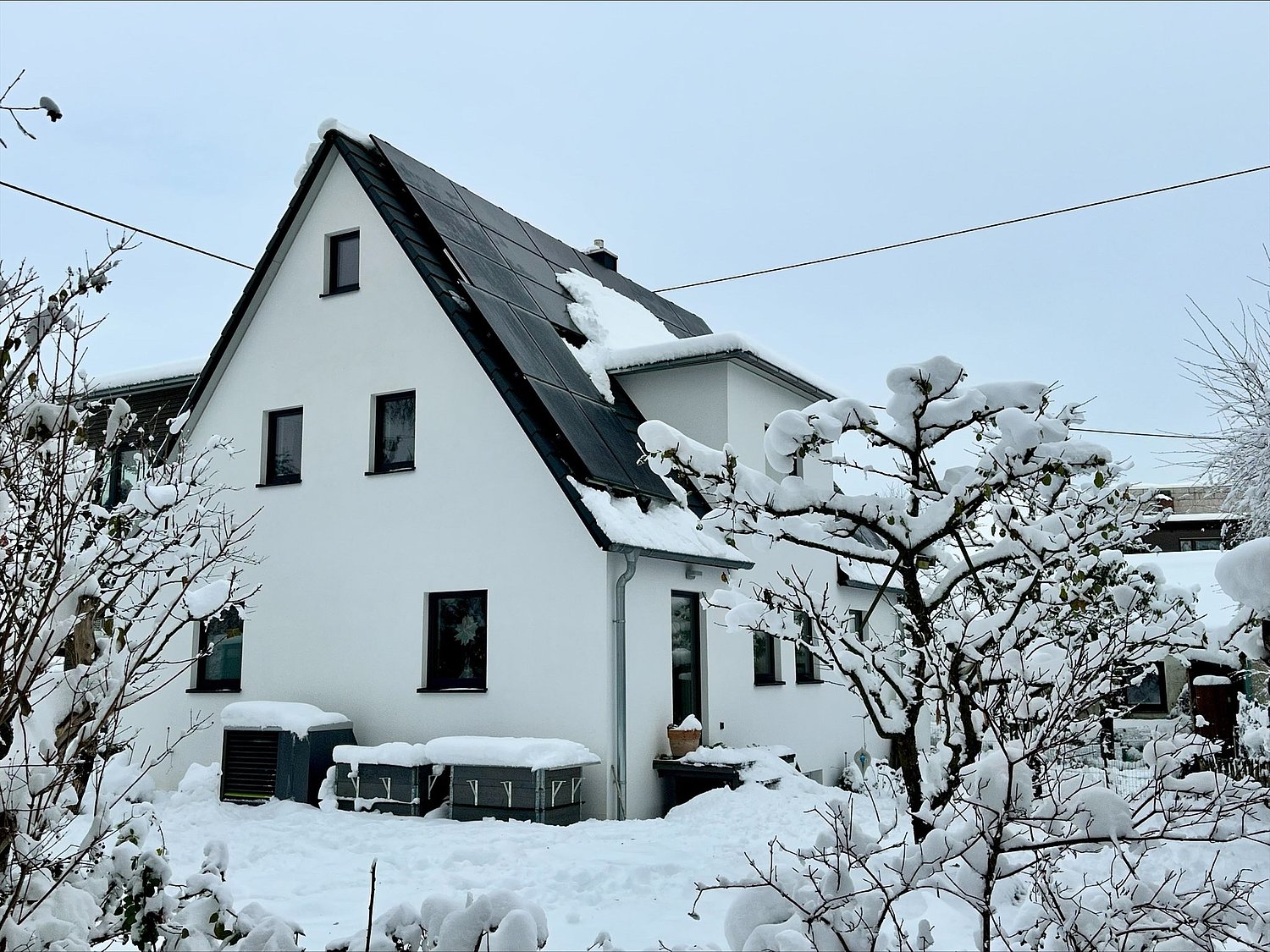Verschneites Haus mit teilweise schneebedeckter PV-anlage