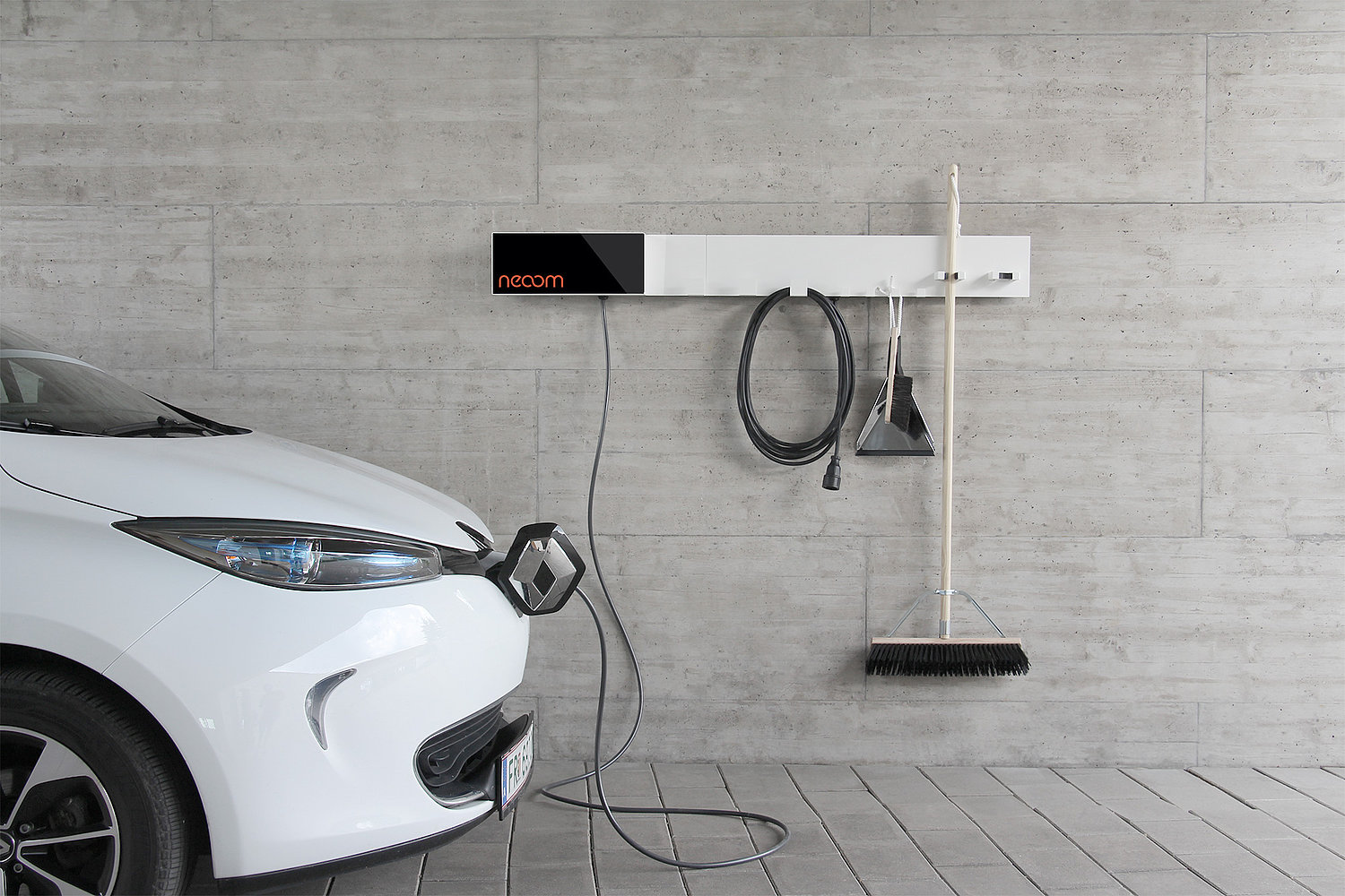 Ein weißes E-Auto links im Bild ist an eine E-Ladesäule von Neoom angeschlossen. Die Konstruktion bietet Platz, um Geräte wie Ladekabel und Besen aufzuhängen